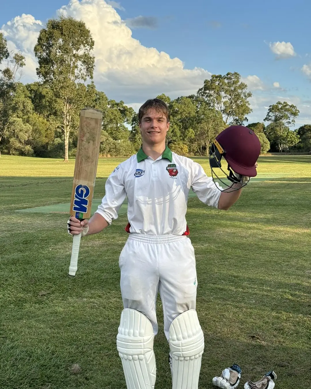 Junior Muddies batter with bat and helmet raised after scoring a century